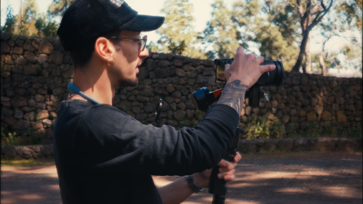 Giuseppe Ciaccio grabando con la cámara al hombro, de perfil, junto a un muro de piedra